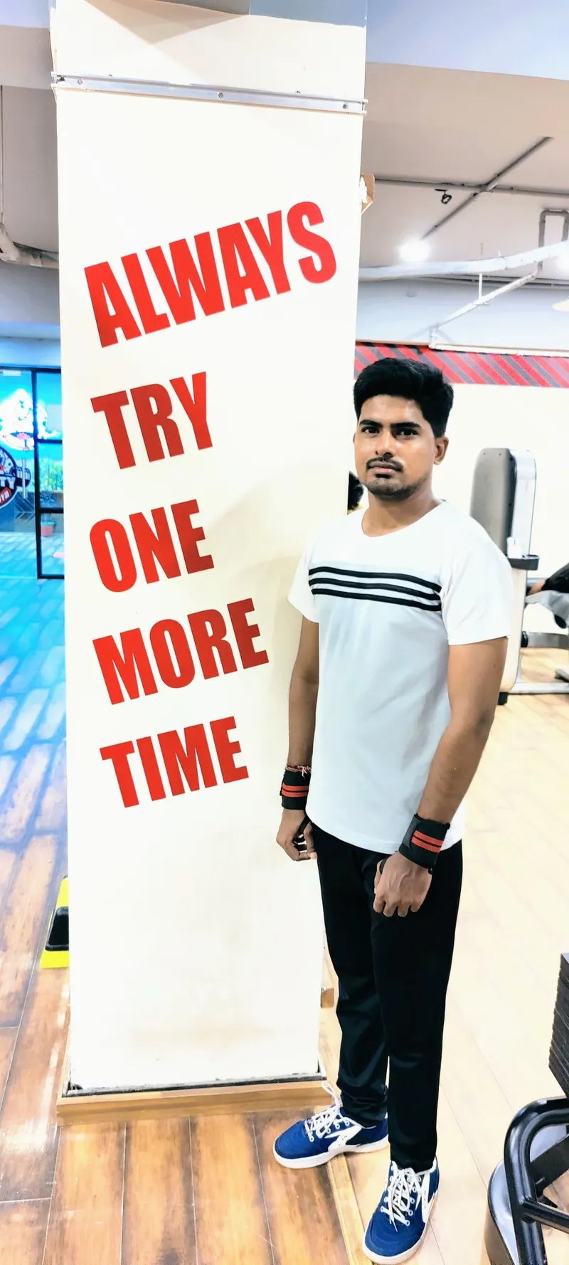 Divyesh at the gym beside a pillar reading "Always try one more time"